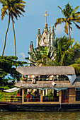 Old church with patinated facade and moored houseboat on a backwaters cruise visitor stop, Alappuzha (Alleppey), Kerala, India, Asia