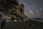 Ein Wanderer findet Schutz in einer Höhle und kocht sein Essen, während die Milchstraße den Himmel des Golfs der Dichter, Gemeinde Ameglia, Provinz La Spezia, Distrikt Ligurien, Italien, Europa, beleuchtet