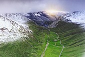 Grüne Wiesen, umrahmt von schneebedeckten Bergen im Frühjahr, Luftbild, Braulio-Tal, Bormio, Valtellina, Lombardei, Italien