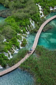 View of people on wooden plank path over pool with waterfalls, Plitvice Lakes National Park, Lika-Senj, Croatia, Europe