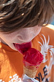 Boy with red tongue enjoys ice cream cone with scoop of raspberry ice cream, Tauberbischofsheim, Baden-Wuerttemberg, Germany, Europe