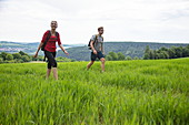 Junge Frau und junger Mann wandern durch Feld, Tauberbischofsheim, Baden-Württemberg, Deutschland, Europa