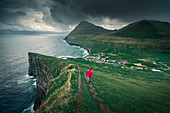 Frau wandert zum Dorf Gjogv auf Eystruoy mit Schlucht, Meer und Bergen, Färöer Inseln