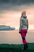 Frau mit Blick auf Klippen von Eysteroy im Sonnenuntergang, Färöer Inseln\n