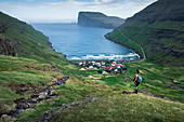 Frau beim Wandern mit Blick auf Dorf Tjørnuvík auf Streymoy auf Färöer Inseln bei Tag\n