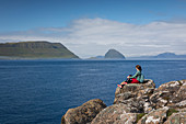 Frau an der Küste mit Blick auf Inseln der Färöer Inseln bei Sonne\n