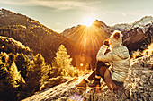 Frau sitzt auf Felsen in Maloja und genießt den Sonnenuntergang, Engadin, Graubünden, Schweiz, Europa