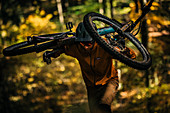 Mountainbiker trägt sein Fahrrad durch herbstlichen Wald