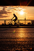 Schattenbild des Mannes, der auf Brücke mit Fernsehturm Berlin im Hintergrund während des Sonnenuntergangs radelt