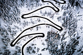 Aerial view of cars on narrow bends of mountain road crossing the snowy forest, Switzerland, Europe