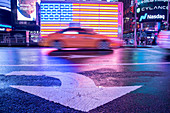 Taxi, das durch eine beleuchtete Flagge der Vereinigten Staaten von Amerika am Times Square, New York City, Vereinigte Staaten von Amerika, Nordamerika verwischt
