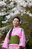 Portrait beautiful young woman in kimono below cherry blossoms