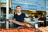 Junger Mann mit großem Fisch in der Ravnkloa Fischhalle, Trondheim, Norwegen