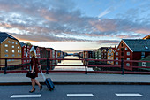 Woman with trolley suitcase on the Bybrua bridge on the Nidelv River, old warehouses along the Nidelva ,, Trondheim, Norway