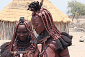 Angola; southern part of Namibe Province; two Muhimba women; traditional hair styling; Strands of hair stuck together with red earth and fluffy fur; Leather chokers; Skin tinted with red earth