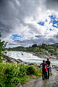 Family gazes at waterfall, The Vefsna River with the Laksfossen waterfall, Norway