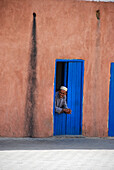 Mann lehnt sich an die Eingangstür in den Straßen der Medina in Marrakesch, Marokko