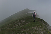 Mann mit Rucksack beim Wandern auf mystischen, nebligen Bergen, Piemont, Italien