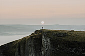 Hiker on cliff at sunrise, Peak District National Park, England