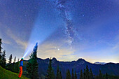 Woman stands at Farrenpoint and shines with lamp on starry sky with Milky Way, Farrenpoint, Mangfall Mountains, Bavarian Alps, Upper Bavaria, Bavaria, Germany