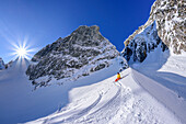 Woman on ski tour takes a break under large rock faces, Zwiesel, Chiemgau Alps, Upper Bavaria, Bavaria, Germany