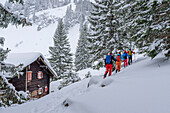 Vier Personen auf Skitour steigen an verschneiter Hütte vorbei zum Tanzeck auf, Tanzeck, Spitzinggebiet, Mangfallgebirge, Bayerische Alpen, Oberbayern, Bayern, Deutschland