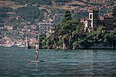 Woman paddles on SUP board in front of Castello della Isola di Loreto castle on island in Lake Iseo in Italy