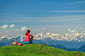 Frau beim Wandern sitzt auf Wiese und blickt auf Hohe Tauern mit Großglockner, vom Rinderfeld, Dachstein, UNESCO Welterbe Hallstatt, Salzburg, Österreich