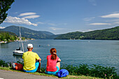 Man and woman while hiking, sitting on the shores of Lake Millstatt, Lake Millstatt, Nockberge Trail, Carinthia, Austria