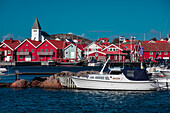 Rote Häuser mit Kirche und Booten im Dorf Skärhamn auf der Schäreninsel Tjörn an der Westküste von Schweden, blauer Himmel mit Sonne\n