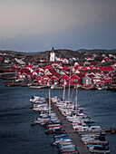 Rote Häuser mit Kirche und Booten im Hafen im Dorf Skärhamn auf der Schäreninsel Tjörn an der Westküste von Schweden, am Abend\n
