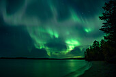 Northern lights in the night sky on the lakeshore in Lapland, Sweden