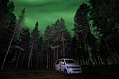 VW Bulli Campervan im Wald unter Polarlichtern im Nachthimmel in Lappland, Schweden\n