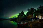 Polarlichter im Nachthimmel am Seeufer mit Hütte und Booten in Lappland, Schweden\n