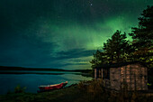 Northern lights in the night sky on the lakeshore with hut and boats in Lapland, Sweden