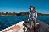Frau sitzt in Paddelboot auf See in Lappland bei Sonne und blauem Himmel\n