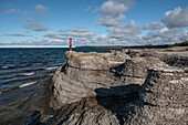 Frau an der Küste der Insel Öland auf Kalksteinfelsen in Schweden bei Sonne und blauem Himmel\n