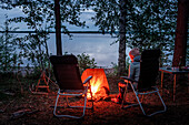 Frau sitzt am Lagerfeuer im Wald am Ufer des Siljansee in Dalarna, Schweden\n