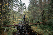 Mann mit Rucksack wandert über kleine Brücke eines Flusses im Wald im Tiveden Nationalpark in Schweden\n