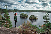 Frau beim Wandern blickt über kleine Inseln im See Stensjön im Tyresta Nationalpark in Schweden\n