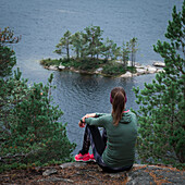 Frau beim Wandern blickt über kleine Insel im See Stensjön im Tyresta Nationalpark in Schweden\n
