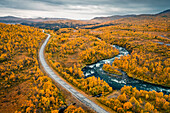 Panoramastrasse Wilderness Road entlang eines Flusses, mit Bergen und Bäumen im Herbst in Jämtland in Schweden von oben\n