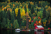 Rotes Bootshaus mit bunten Bäumen am See entlang der Wilderness Road im Herbst in Jämtland in Schweden\n