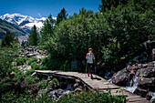 Frau wandert auf Brücke mit Bach am Morteratsch Gletscher im Engadin in den Schweizer Alpen im Sommer\n