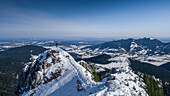 Mann steht auf Gipfel des Teufelstaettkopf im Winter auf Skitour und schaut über das verschneite Tal der Ammergauer Alpen in Bayern im Winter