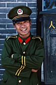 Porträt eines lächelnden chinesischen Soldaten in Uniform, der mit verschränkten Armen steht, China