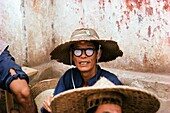 Man wearing a straw hat and black rimmed glasses sitting outside a building, China