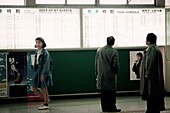 Woman walking away from train schedule as two men check schedule, Tokyo, Japan