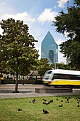 USA, Texas, Dallas, Train speeding past pigeons in grassy area, Fountain Place building in background
