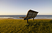 Empty park bench on grassy bank overlooking beach in early morning